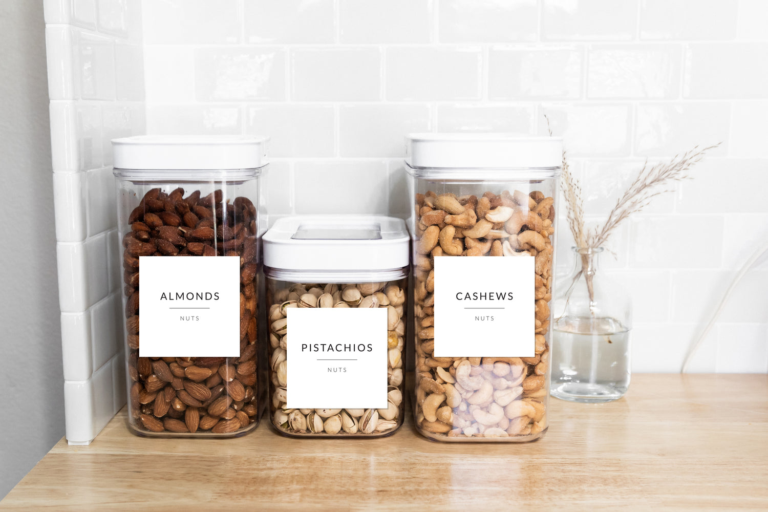Organised pantry containers with Savvy & Sorted White Minimalist Pantry Labels filled with nuts on a white subway tile kitchen counter