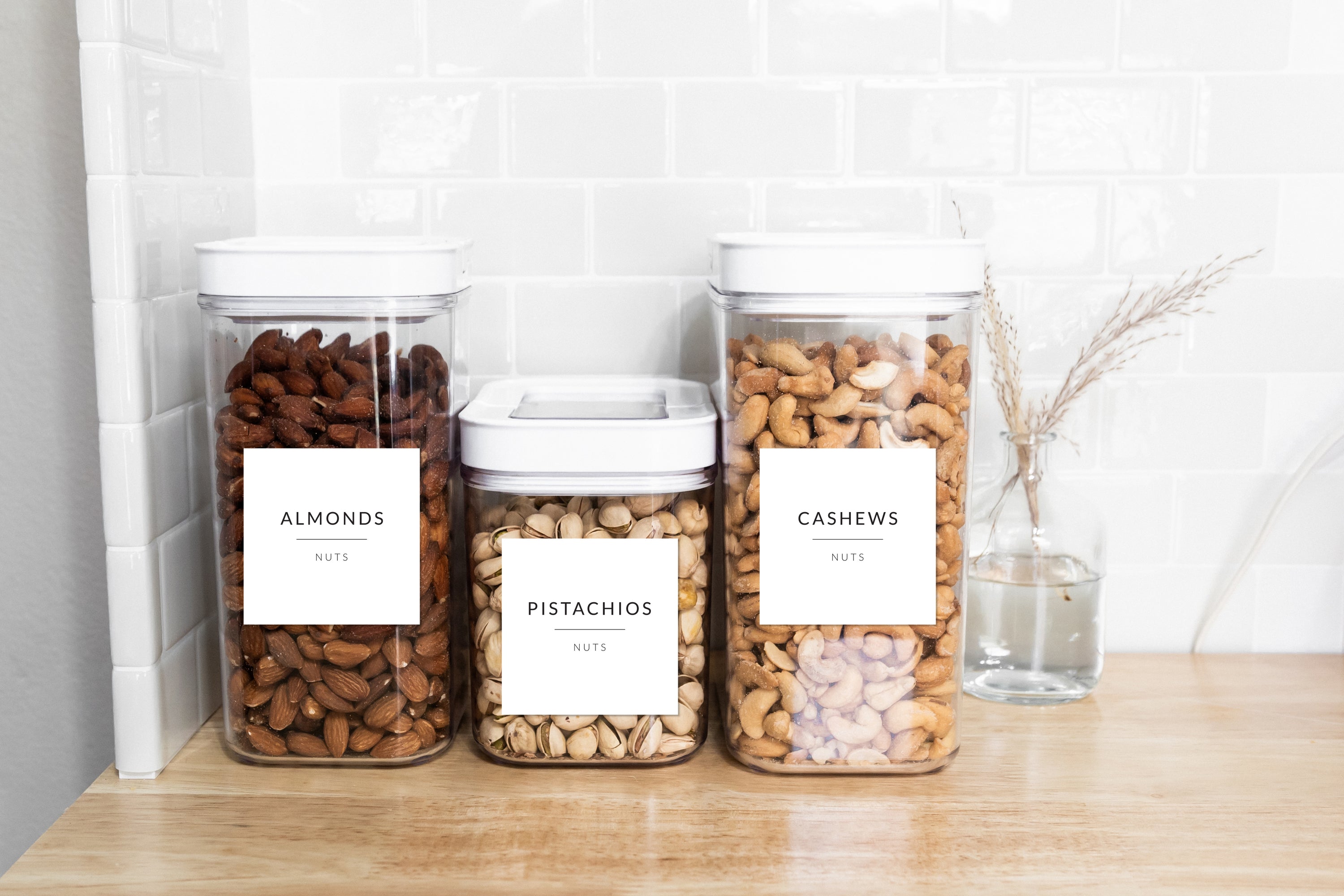Organised pantry containers with Savvy & Sorted White Minimalist Pantry Labels filled with nuts on a white subway tile kitchen counter