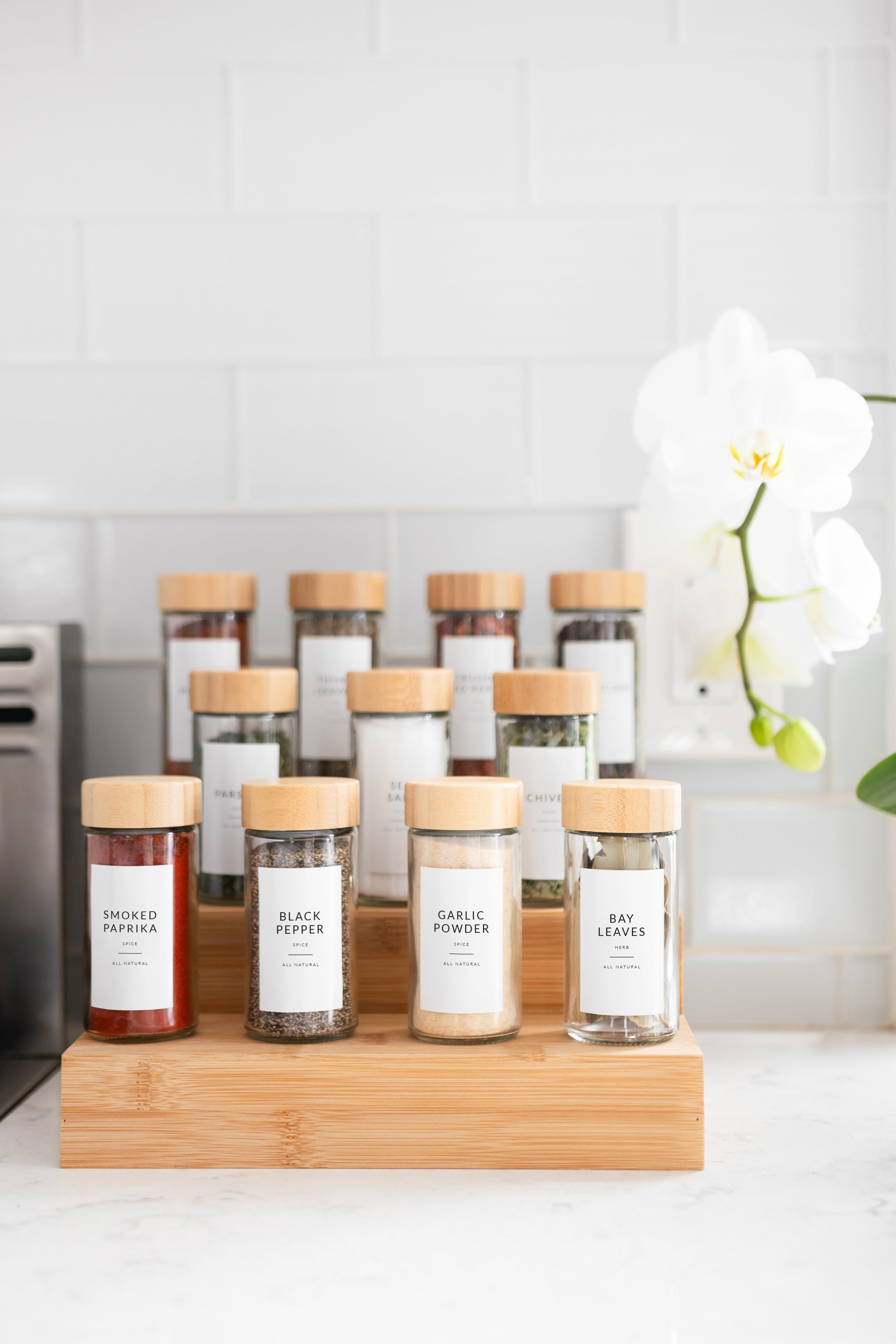 Tiered bamboo spice rack with glass jars and white minimalist spice labels on white marble counter - Savvy & Sorted