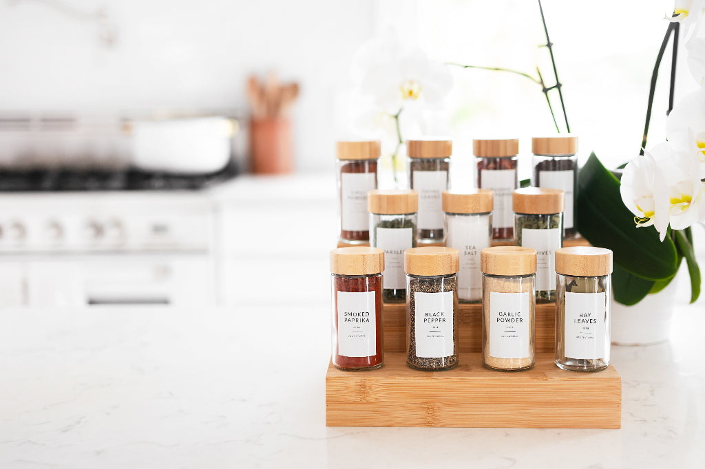 Round bamboo lid glass spice jars stacked on a tiered rack next to a white orchid on marble counter