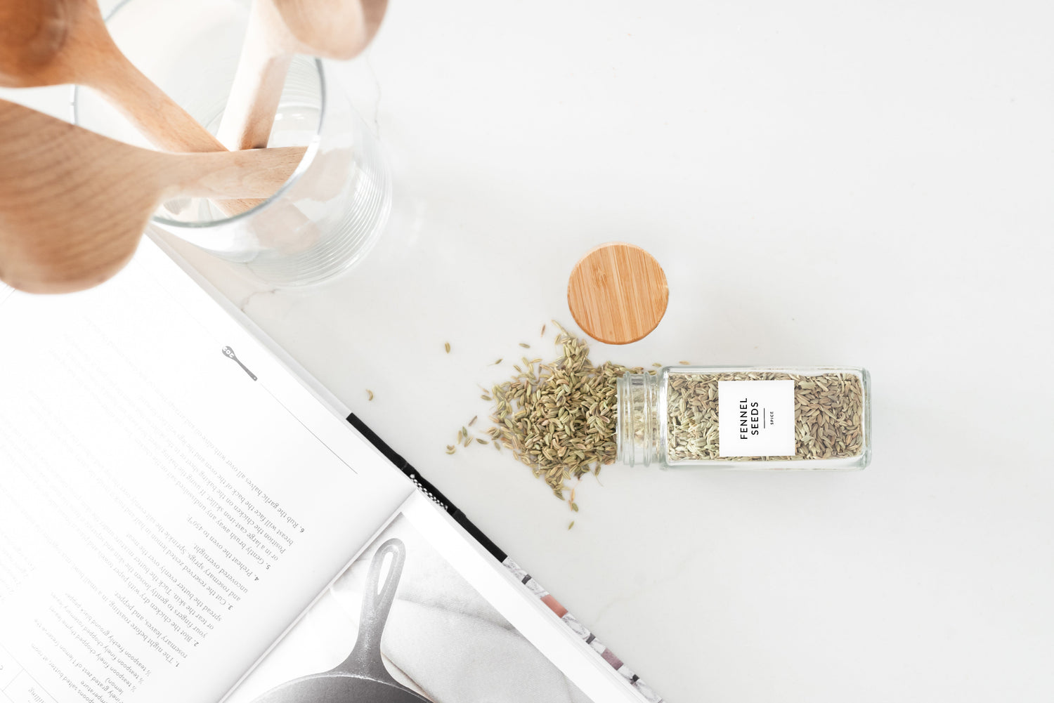 Bamboo rectangle spice jars styled with an open cookbook and wooden utensils on a white marble surface