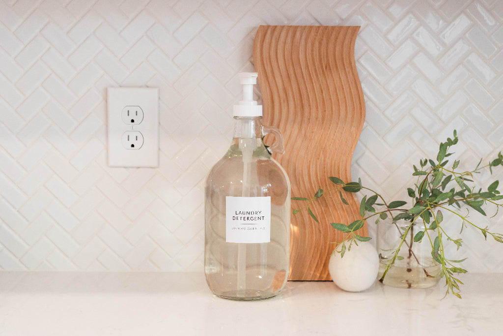 Labeled laundry detergent bottle on a white kitchen counter with herringbone tile