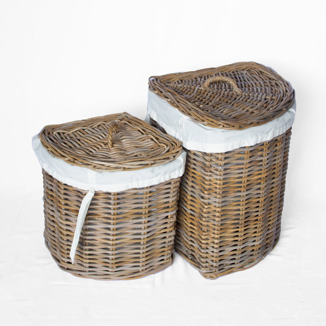 Two woven wicker laundry hamper baskets with lids, one small and one large, both lined with white fabric and shown on a white background.