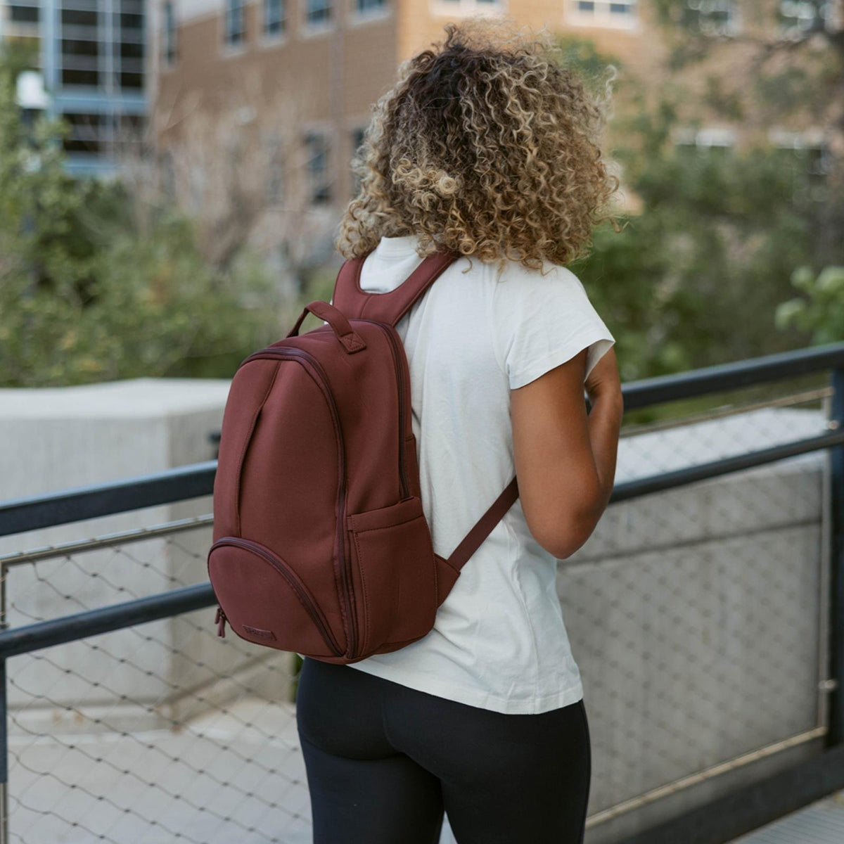 Person with a brown backpack walking outdoors on a city street.