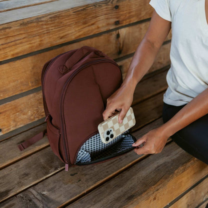 Person placing a phone into a brown backpack on a wooden surface