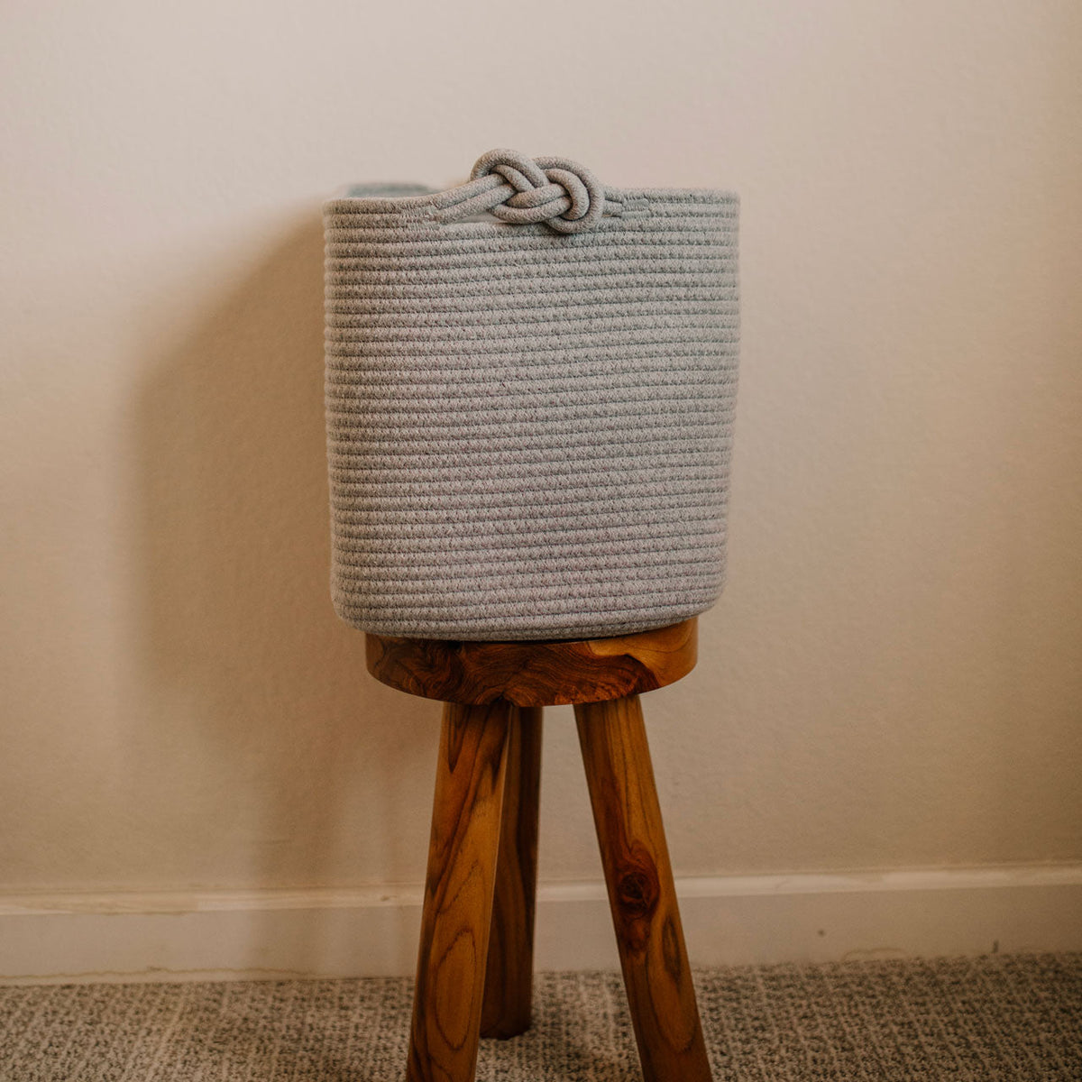 Gray woven basket on a wooden stool against a beige wall.