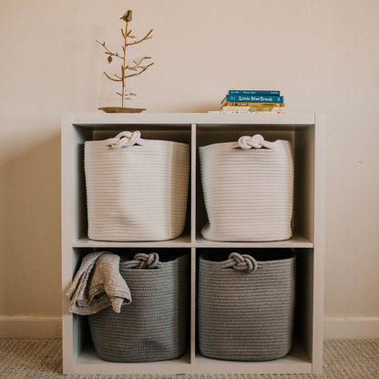 White and gray woven baskets on a wooden shelf against a beige wall.