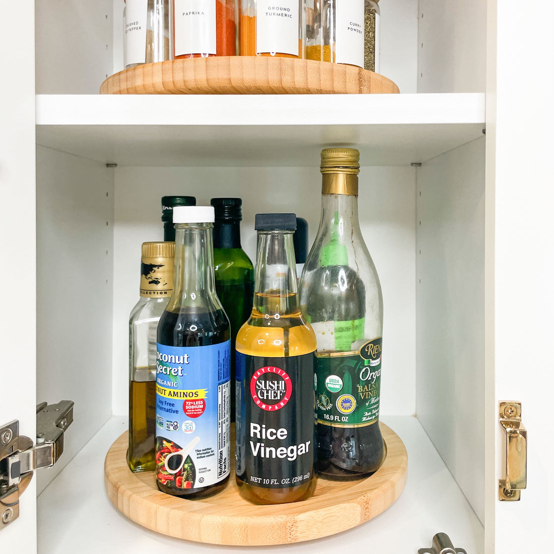 Bottles of various condiments on a wooden shelf inside a kitchen cabinet.