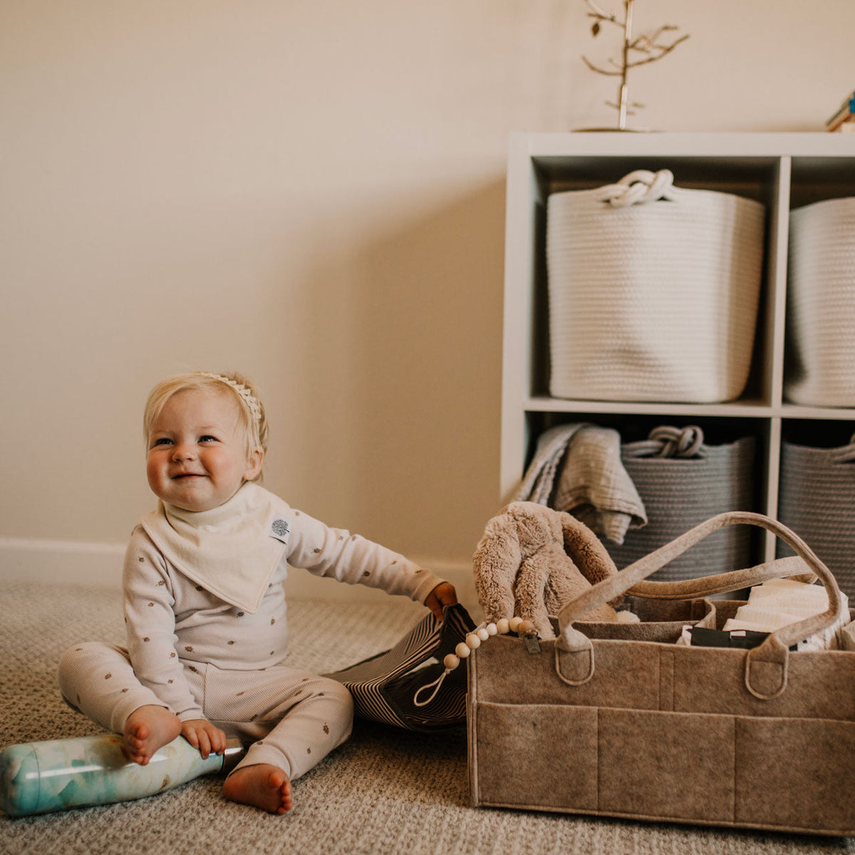 Child sitting on the floor next to a storage basket with toys in a room.