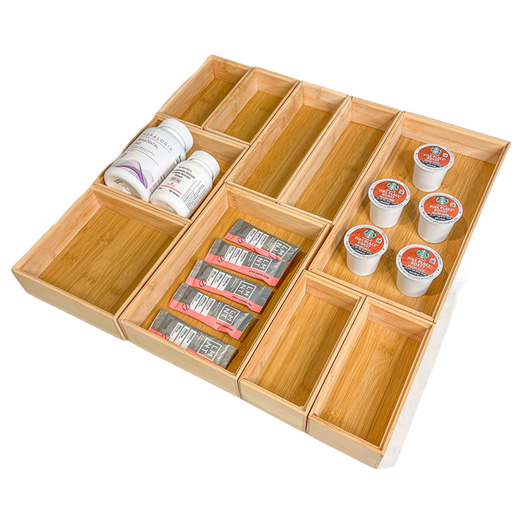 A light natural bamboo compartment organizer tray set, shown filled with various household items including supplement bottles, coffee pods, and packaged snacks, on a clean white background.