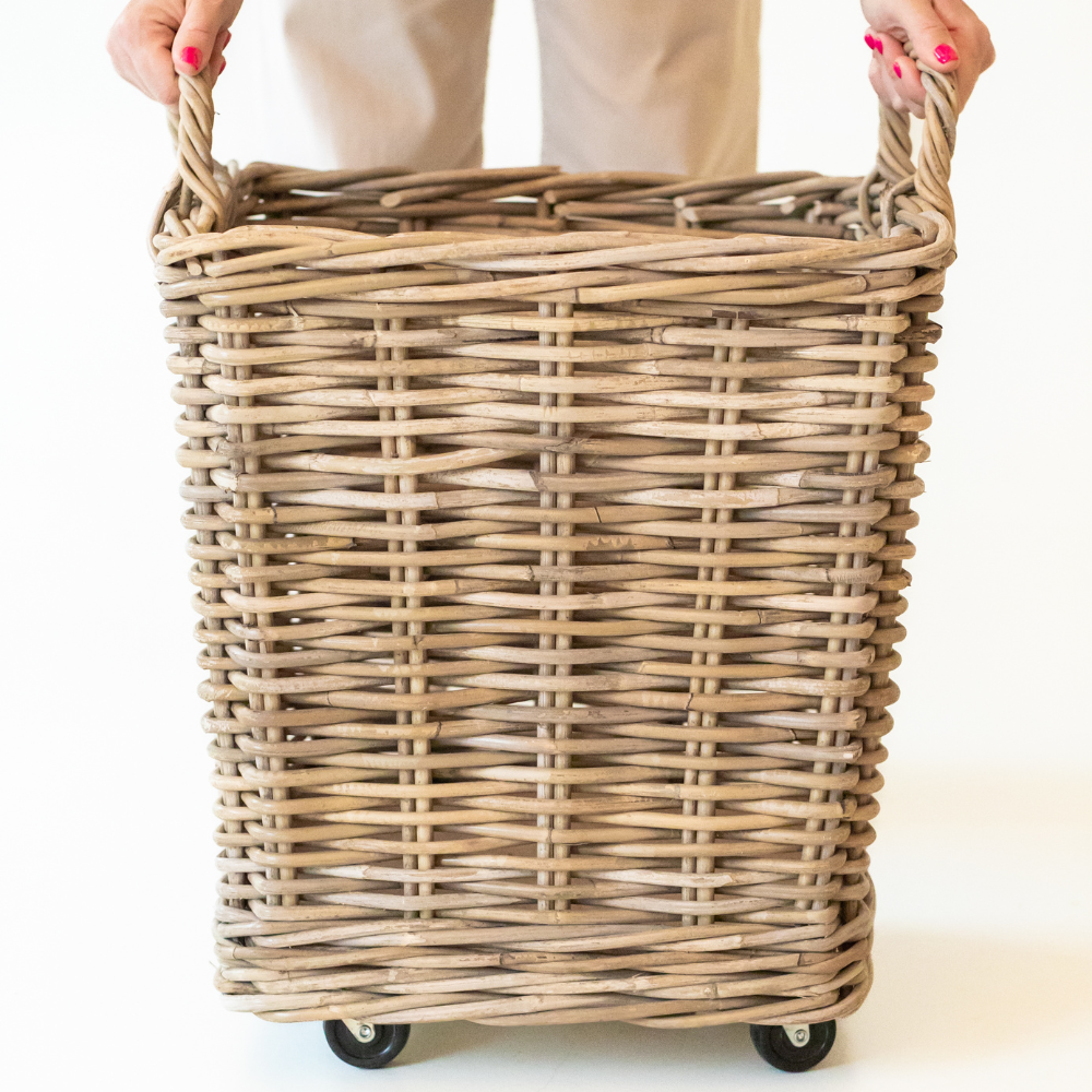 Wicker laundry basket with wheels held by a person on a white background