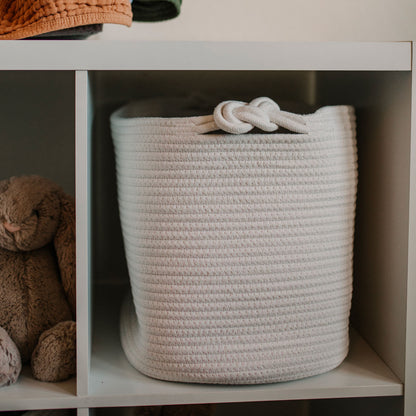 Woven basket with a knot handle on a shelf with a teddy bear and clothes in the background