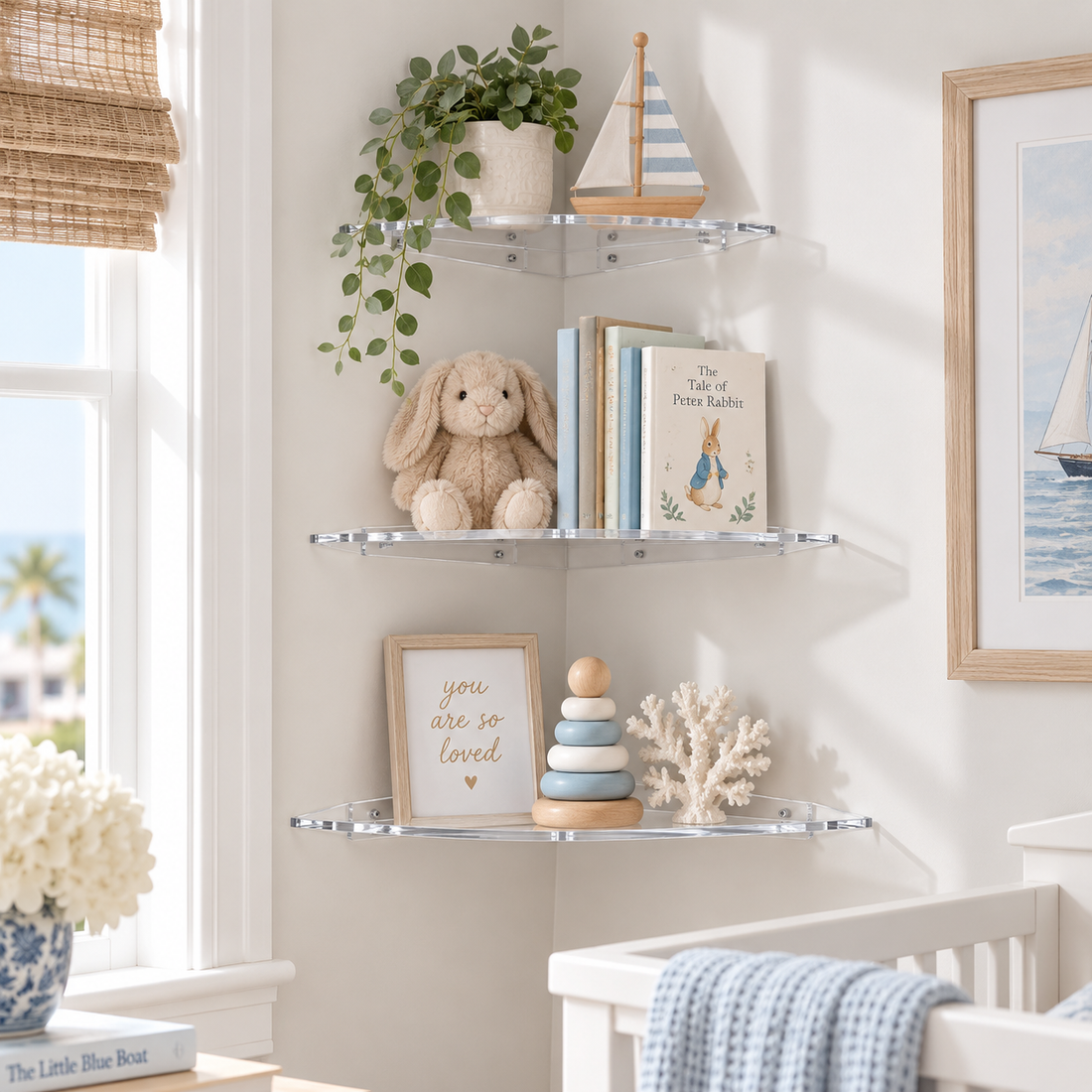 Three clear acrylic corner wall shelves mounted on a light beige wall in a nursery setting, styled with a green trailing plant, a wooden sailboat, a plush bunny, books, a framed sign, and a small stack toy.