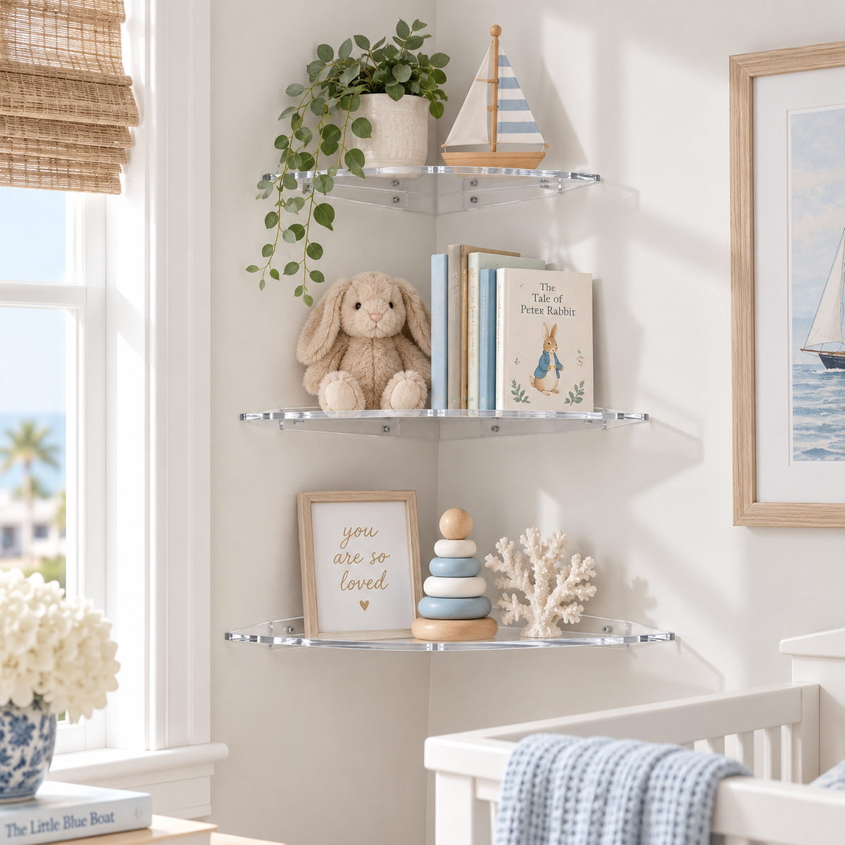 Three clear acrylic corner wall shelves mounted on a light beige wall in a nursery setting, styled with a green trailing plant, a wooden sailboat, a plush bunny, books, a framed sign, and a small stack toy.