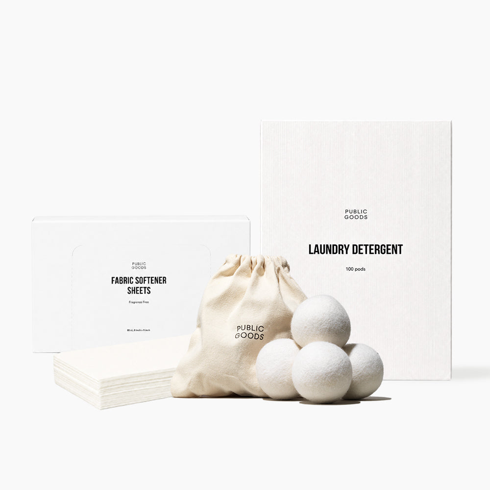 Public Goods laundry detergent and fabric softener set, featuring white boxes, a beige fabric drawstring bag, and five textured white detergent balls on a clean white background.