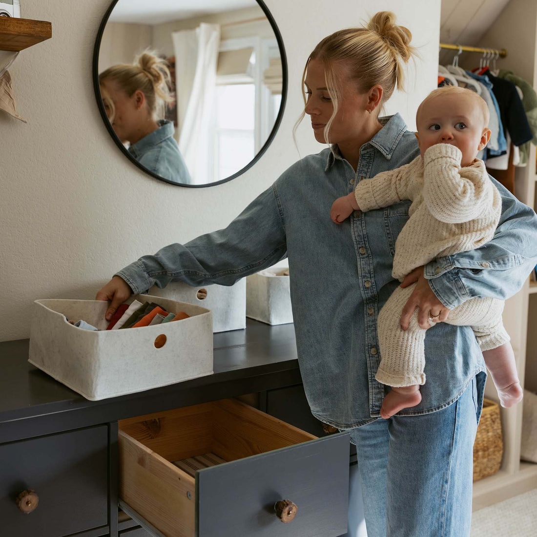 Woman holding a baby while organizing items in a room.